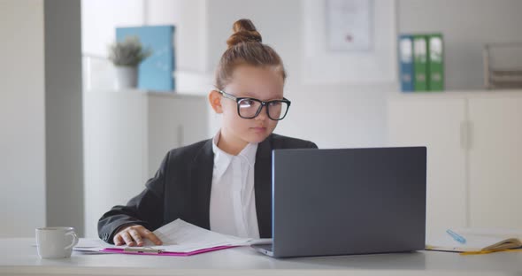 Concentrated Little Girl Boss Working on Laptop and Doing Paperwork in Office