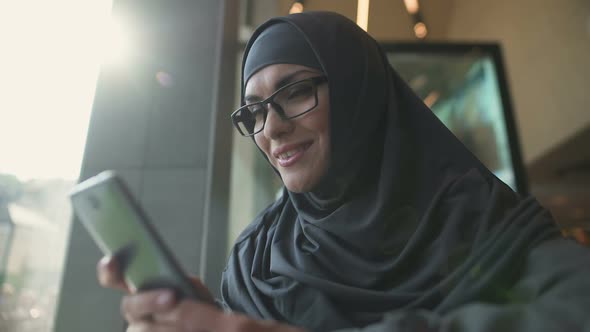 Smiling Arabic Lady in Cafe Chatting on Phone, Application for Online Shopping