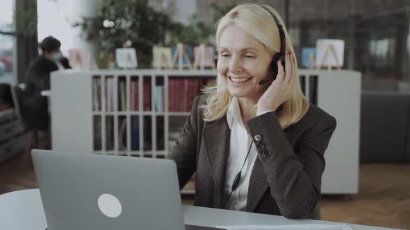 Middleaged Business Woman with Headset Working on Laptop in the Office and Advises Online