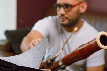 blurred man sitting with a bassoon turning the sheet music page on the music stand. focus on paper
