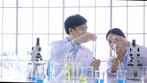 Young Asian Female Scientist Doing Research in Laboratory Wearing Lab Coat and Gloves with Colleague