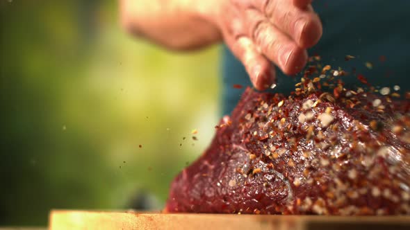 Chef Is Sprinkling Pepper And Salt On Fresh Beef Meat On A Wooden Cutting Board In Slow Motion