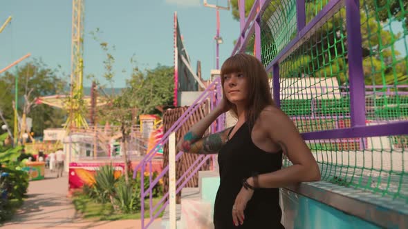 Portrait of a tanned young woman with tattoo sleeve posing near a fence.