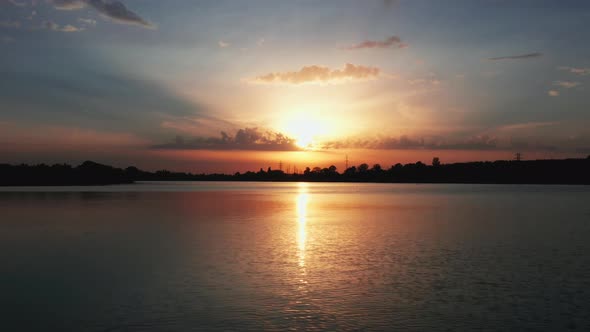 Lake at sunset with dramatic sky. Backward drone flight over the water surface.