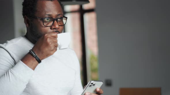 Serious man drinking coffee and texting by phone