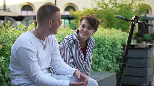 Portrait of Happy Caucasian Woman Talking with Man and Looking at Camera Smiling Sitting on Urban