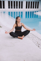 Young woman sitting and meditating on the floor by blue swimming pool.  - PhotoDune Item for Sale