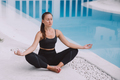 Slim sporty woman in sportswear meditating in the morning by blue swimming pool. - PhotoDune Item for Sale