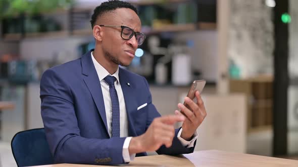 African Businessman Reacting to Failure on Smartphone in Office