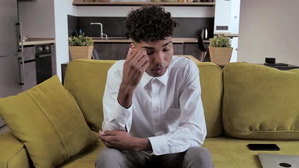 Tired Mixed Race Guy Sitting On Sofa Feels Pain In His Eyes