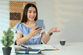 Smiling young asian woman chatting with client online on smart phone and using laptop - PhotoDune Item for Sale