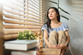 Pensive young woman sitting on chair embracing knees looking out window. - PhotoDune Item for Sale