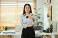 Portrait of millennial female entrepreneur standing in front of her desk and smiling at camera. - PhotoDune Item for Sale