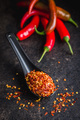 Dry chili pepper flakes. Crushed red peppers in spoon on black table. - PhotoDune Item for Sale