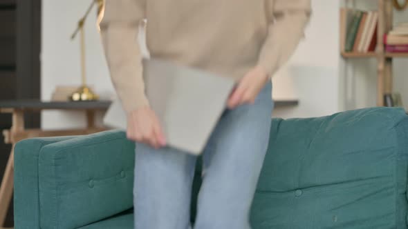 Young Woman with Laptop Coming Back, Sitting on Sofa 