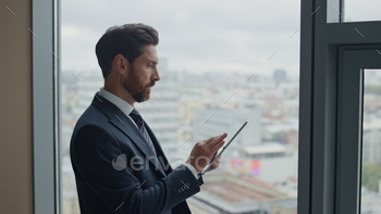  standing at office window with great cityscape close up. Bearded confident ceo manager thinking on career growth new project holding tab computer.