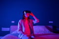 Relaxed smiling young woman in vr glasses is playing video games in dark room. - PhotoDune Item for Sale