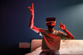 Young African American man sitting on bed under red neon light using futuristic metaverse VR headset - PhotoDune Item for Sale