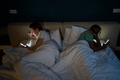 Family diverse couple in bed with smartphones husband and wife turned away from each other. - PhotoDune Item for Sale