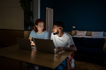 Serious multiethnic freelancers guy and girl working on laptops in dark sitting at desk at home. - PhotoDune Item for Sale