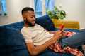 Relaxed smiling african american smiling man sits on couch looks at smartphone at home. - PhotoDune Item for Sale