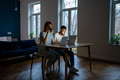 Young modern freelancing couple sitting at table in living room working from home together - PhotoDune Item for Sale
