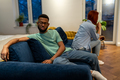 Unhappy young interracial couple sit separately on sofa at home not talking after fight - PhotoDune Item for Sale