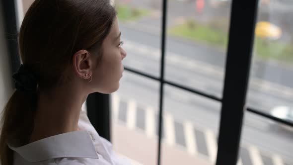 A young woman looks out of the window at passing cars on the road near her house