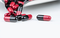 Red-black antibiotic capsule pills with blur drug tray on white table. Antibiotic drug smart use. - PhotoDune Item for Sale