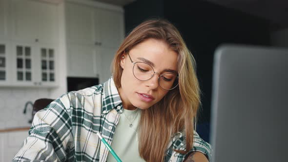 Young Focused Blonde Woman Watching Lesson Online or Reading Seminar and Writing Notes Studying