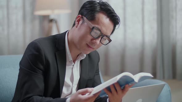 Close Up Of Asian Businessman In Jacket And Shorts Reading A Book After Working With A Laptop
