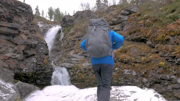 Tourist with a Backpack Climbs Up on a Rock at a Mountain Waterfall. He Reached the End of the Route