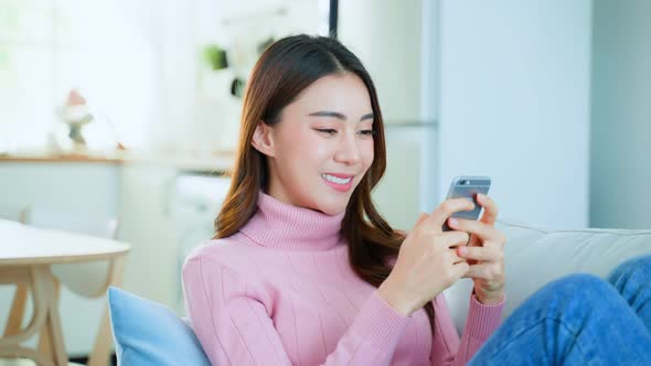 Asian beautiful woman sit on sofa and chat on mobile phone in living room in house during holiday.
