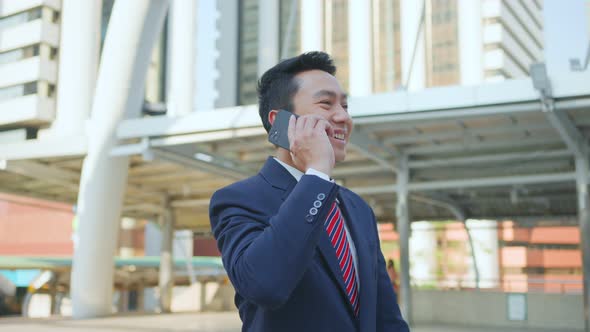 Asian manager smart businessman using smartphone, walking standing outdoor in city with smile face.