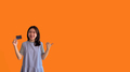 Asian woman holding credit card and thumbs up on orange background - PhotoDune Item for Sale