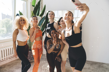 Group of positive sportswomen taking selfie in gym