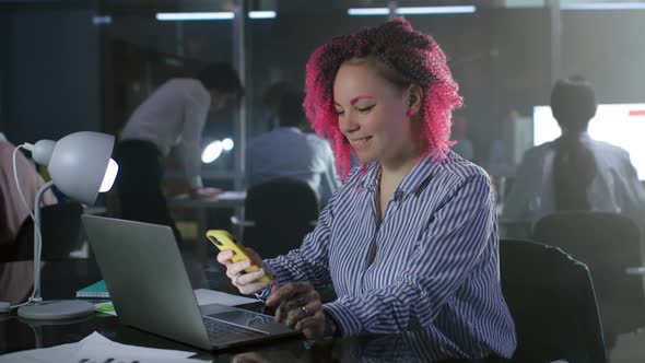 Office Manager with Pink Hair Work on Laptop and Use Smartphone Late in Office