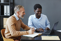 Side view mature businessman using laptop with colleague at desk in office - PhotoDune Item for Sale