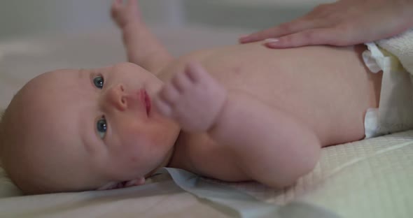 Cute Newborn Baby with Diaper Lying on Bed and Mother Caress His Tummy