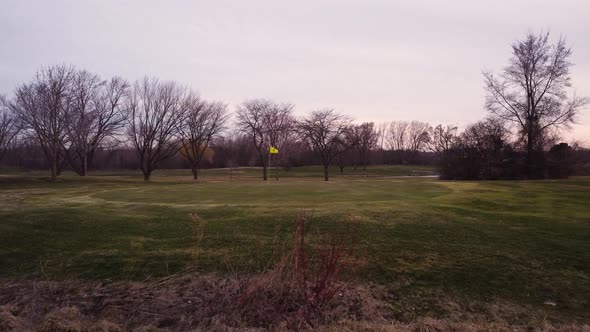 Yellow flag on a Golf course green, wide shot aerial tracking forwards over a water obstacle. Trees