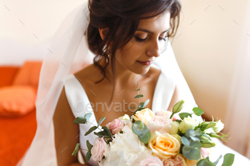 Morning of bride. Beautiful smiling brunette bride in white dress with wedding bouquet in her hands.