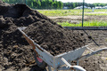 A heap of pure black earth lying in the yard next to the fence, visible shovel and full wheelbarrow. - PhotoDune Item for Sale