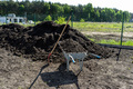 A heap of pure black earth lying in the yard next to the fence, visible shovel and full wheelbarrow. - PhotoDune Item for Sale