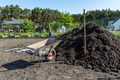 A heap of pure black earth lying in the yard next to the fence, visible shovel and empty wheelbarrow - PhotoDune Item for Sale