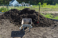 A heap of pure black earth lying in the yard next to the fence, visible shovel and empty wheelbarrow - PhotoDune Item for Sale
