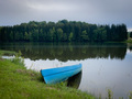 One blue wooden boat and a lake surrounded by forest of coniferous trees on a cloudy summer day - PhotoDune Item for Sale