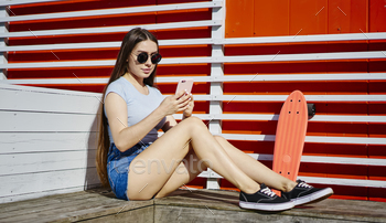 Skater with penny board using smartphone device for online chatting