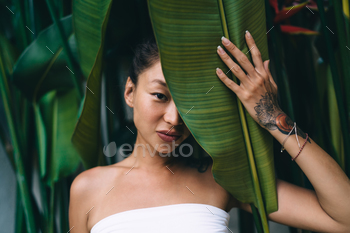 Asian woman with tattoo and palm leaf on half of face