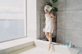 Girl wrapped in towels stepping in bath with water in modern sunny bathroom. Self-care, spa, hygiene - PhotoDune Item for Sale