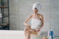 Woman wrapped in towel massages hip with massaging brush in bathroom. Cellulite treatment, body care - PhotoDune Item for Sale